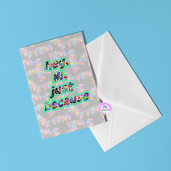 The Hey, Hi, Just Because Greeting Card by My Store features colorful text and multicolored squiggles. It has a blank interior for personalization and includes an eco-friendly card peeking out of a white envelope on a light blue surface.