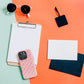 Flat lay of a clipboard, sunglasses, blank tag, two empty cards (one white, one black), and a smartphone in an Iced Vovo MagSafe iPhone Case by My Favourite Colour is Rainbow on a vibrant green and orange background.