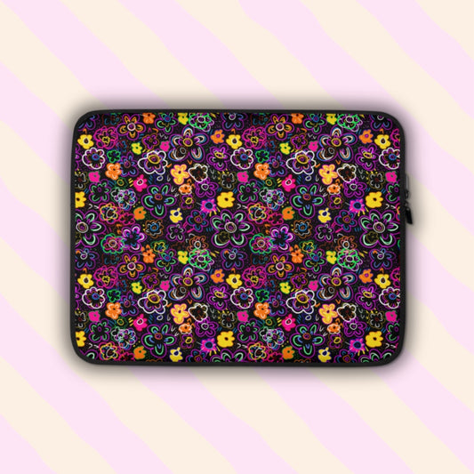 Check out the In the Midnight Garden Laptop Sleeve by My Favourite Colour is Rainbow. It features a vibrant floral pattern with pink, yellow, green, and orange flowers on a dark background. The sleeve is padded and lined for added style and protection.  Shown on a light pink and yellow background.