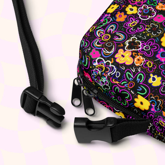 Close-up of My Favourite Colour is Rainbows In the Midnight Garden mini crossbody bag with vibrant multicoloured flowers on a dark background, featuring black zippers and an adjustable strap with plastic buckles.