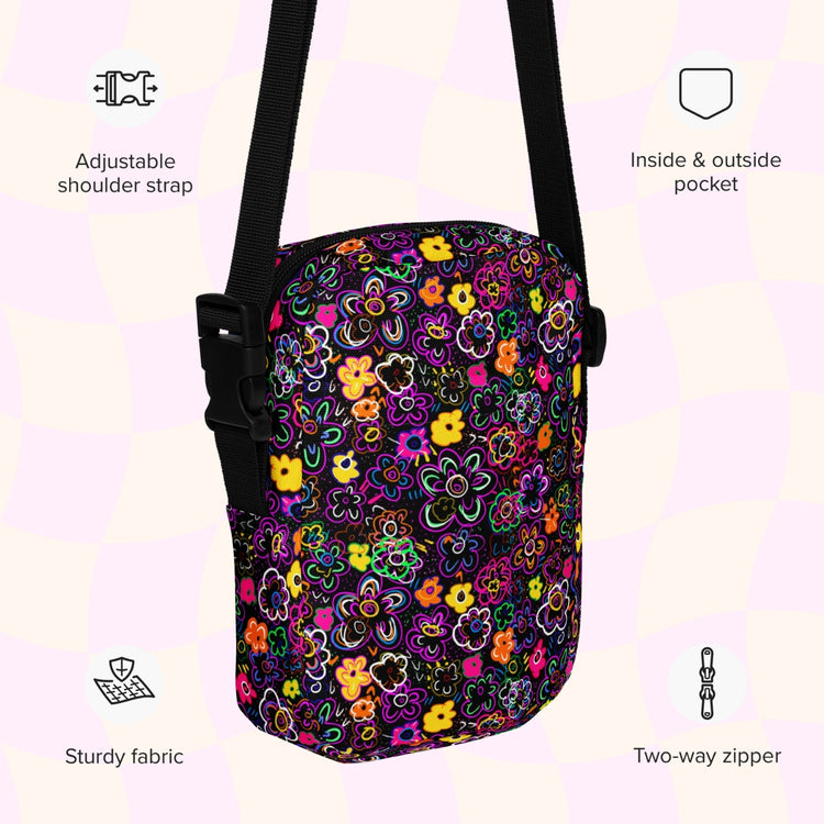 An infographic highlighting features of the In the Midnight Garden Mini Crossbody Bag by My Favourite Colour is Rainbow: adjustable shoulder strap, inside and outside pocket, sturdy canvas fabric and a two-way zipper.  The bag is decorated with a vibrant floral pattern with pink, orange, yellow, and green on a black background.  