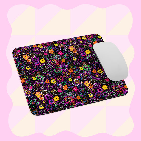 The In the Midnight Garden Mouse Pad by My Favourite Colour is Rainbow showcases a vibrant floral design against a light pink and yellow checkered background, with a white computer mouse placed on the pads right side.