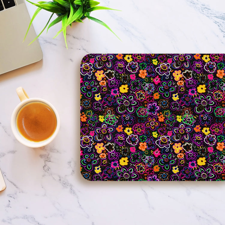 The In the Midnight Garden Mouse Pad by My Favourite Colour is Rainbow sits near a coffee cup and small green plant on a marble surface, creating a cozy workspace vibe with its colorful floral pattern.