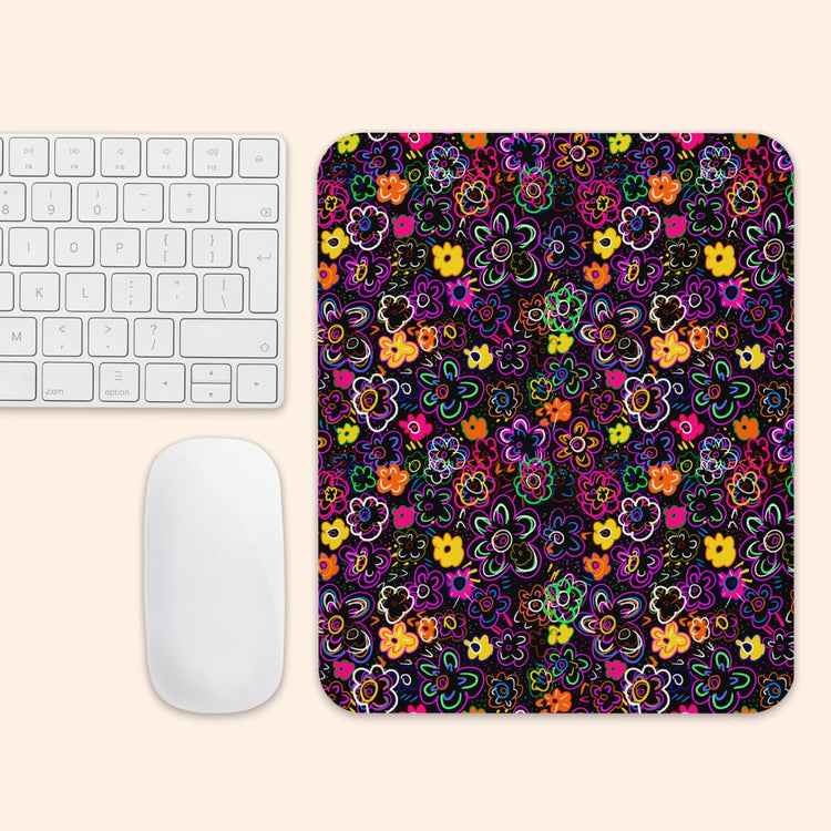 The In the Midnight Garden Mouse Pad by My Favourite Colour is Rainbow showcases vibrant pink, yellow, orange, and purple floral patterns on a black background beside a white keyboard and mouse on a light beige surface.