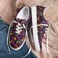 The In the Midnight Garden Canvas Sneakers by My Favourite Colour is Rainbow, with vibrant floral designs on a dark background, sit atop a folded pink sweater and denim jeans.  The sneakers have white soles and laces.