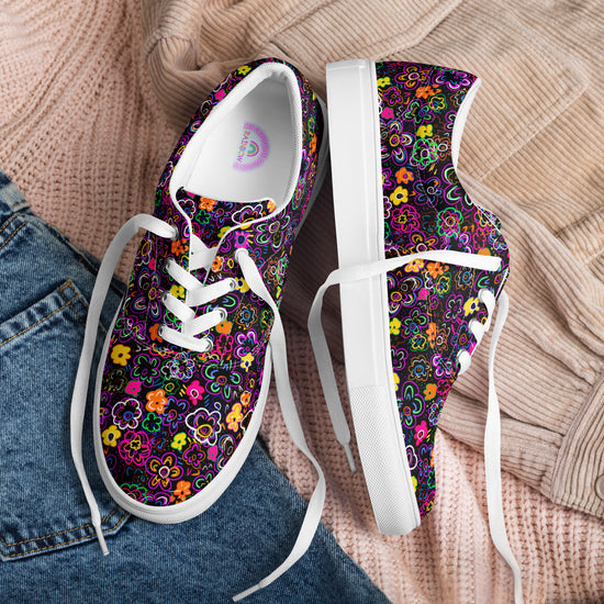 The In the Midnight Garden Canvas Sneakers by My Favourite Colour is Rainbow, with vibrant floral designs on a dark background, sit atop a folded pink sweater and denim jeans.  The sneakers have white soles and laces.