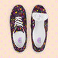 Two In the Midnight Garden Canvas Sneakers by My Favourite Colour is Rainbow display a vibrant floral print on black canvas. One shoe stands upright, showcasing laces; the other lies on its side, revealing the inner sole label. They feature breathable lining for comfort against a light peach background with pink diamond shapes.