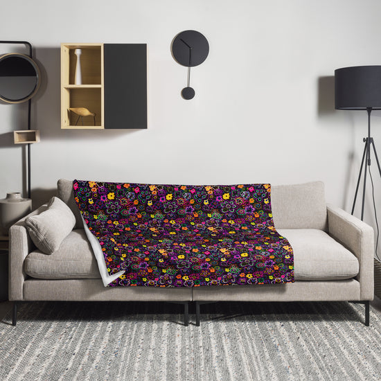 A beige sofa adorned with the In the Midnight Garden throw blanket by My Favourite Colour is Rainbow featuring a vibrant floral pattern. The room includes a wall-mounted cabinet, black floor lamp, modern clock, and patterned rug on the gray floor.