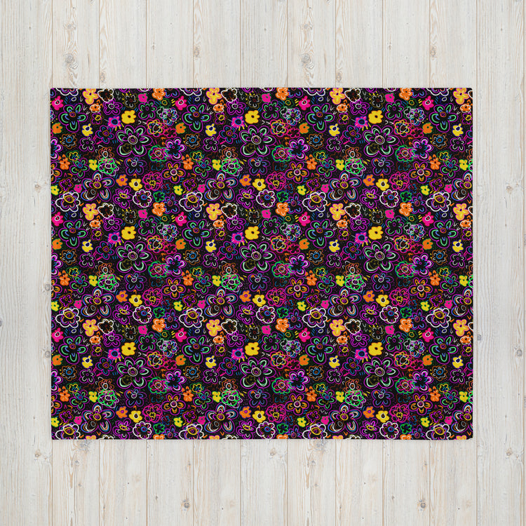 The In the Midnight Garden Throw Blanket by My Favourite Colour is Rainbow showcases a vibrant, cozy fabric with multicolored flowers in shades of purple, orange, yellow, red, and blue on a dark background—ideal for styling on a light wood surface.