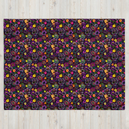 The In the Midnight Garden Throw Blanket by My Favourite Colour is Rainbow boasts colorful, intricate floral patterns in purple, pink, yellow, green, and orange against a dark background. It adds a vibrant touch to any light wooden floor with its cozy fabric warmth.