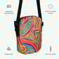 An infographic highlighting features of the Karma Kaleidoscope Mini Crossbody Bag by My Favourite Colour is Rainbow: adjustable shoulder strap, inside and outside pocket, sturdy canvas fabric and a two-way zipper.  My Karma Kaleidoscope painting reproduced on the bag features a lively pattern of bold pink, orange, blue, and green swirls and geometric shapes.