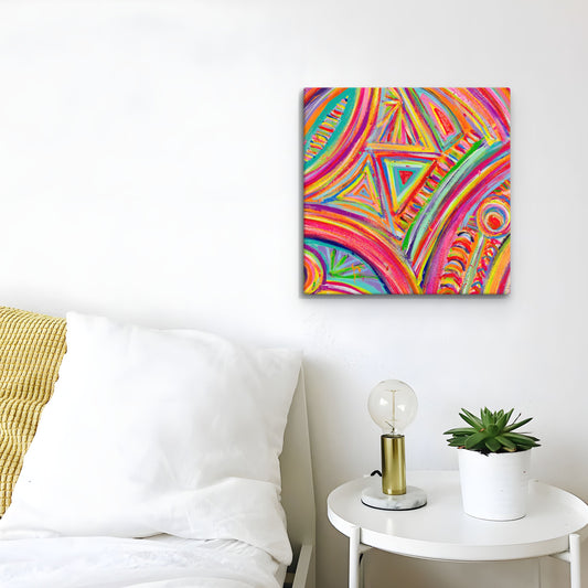 A bedroom with a white bed and side table holding a lamp and potted plant features the Karma Kaleidoscope Canvas Artwork by My Favourite Colour is Rainbow, adding energy with its vibrant, geometric abstract patterns on the wall.