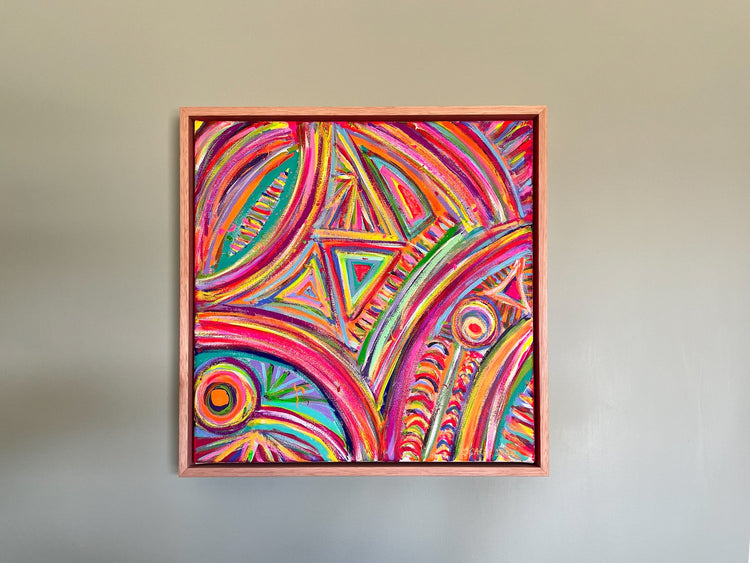 The Karma Kaleidoscope Framed Original Painting by My Store features vibrant swirls, triangles, and circles in pink, purple, orange, and yellow hues. Elegantly framed in simple wood, it is displayed on a plain light gray wall.