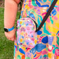 Clad in a vibrant dress and blue watch, a colourful woman enjoys the outdoors with a Kiwi to Aussie Mini Crossbody bag by My Favourite Colour is Rainbow. 