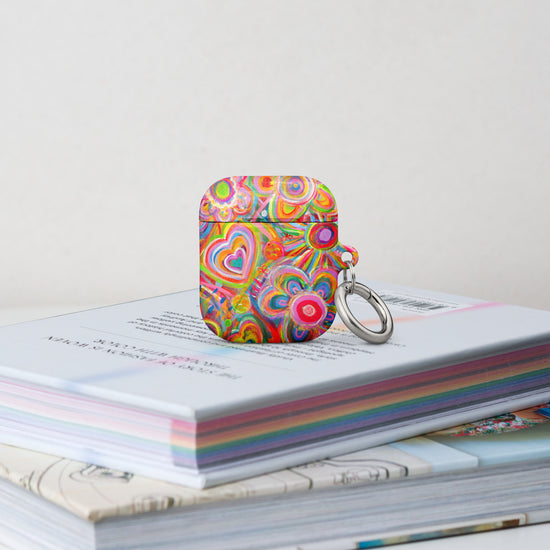 The Love in Neon Airpods Gen 1 Case stands on a stack of books.  It features vibrant heart and floral patterns and swirling rainbow designs. 