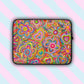 The Love in Neon Laptop Sleeve by My Favourite Colour is Rainbow features a splash-resistant, scratch-proof design with a vibrant pattern of hearts and flowers, enhanced by swirling lines and colourful dots. Its shown on a pink and blue striped backdrop.