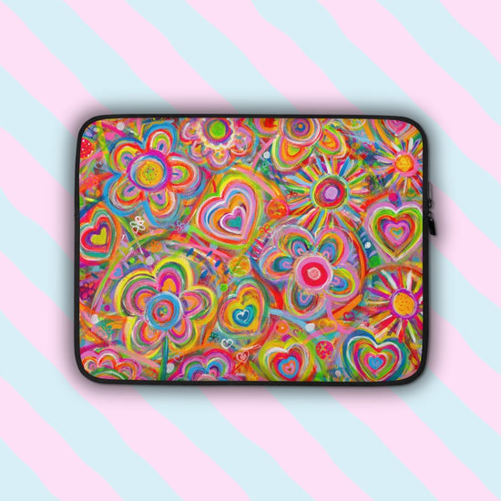 The Love in Neon Laptop Sleeve by My Favourite Colour is Rainbow features a splash-resistant, scratch-proof design with a vibrant pattern of hearts and flowers, enhanced by swirling lines and colourful dots. Its shown on a pink and blue striped backdrop.