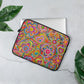 The 13 inch Love in Neon Laptop Sleeve by My Favourite Colour is Rainbow features a vibrant design of multicoloured flowers, hearts and suns. It rests on a grey surface next to green leaves with a laptop partially inside.