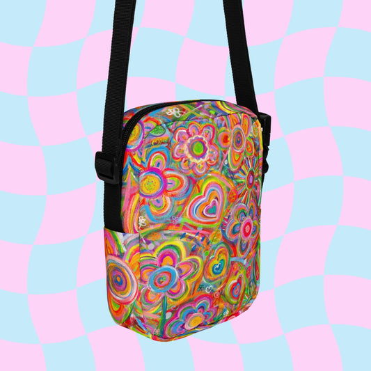 The Love in Neon Mini Crossbody Bag by My Favourite Colour is Rainbow features a psychedelic floral, heart, and spiral design on a pastel pink and blue checkered background, hanging from an adjustable black strap and made from water-resistant material for your adventures.