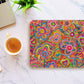 The Love in Neon Mouse Pad by My Favourite Colour is Rainbow boasts an abstract design with hearts and flowers, set on a marble surface beside an open laptop, coffee cup, and green plant.