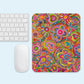 A white keyboard and mouse sit next to the Love in Neon Mouse Pad by My Favourite Colour is Rainbow, featuring a vibrant abstract floral design with multicolored flowers and hearts on a light blue background.