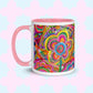 The Love in Neon Mug by My Favourite Colour is Rainbow features my Love in Neon painting with bold floral and heart patterns in vibrant pink, yellow, blue, and green. It has a light pink handle and interior.