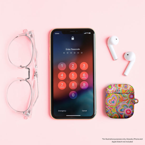 On a pink surface, a smartphone with a passcode screen sits beside clear eyeglasses, wireless earbuds, and the vibrant Love in Neon AirPods case by My Favourite Colour is Rainbow, featuring heart patterns.