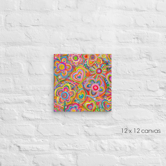 Love in Neon Canvas Artwork by My Favourite Colour is Rainbow features vibrant, abstract art with colorful flowers and hearts on a white textured brick wall. This 12x12 inch piece bursts with pink, orange, and blue swirls.