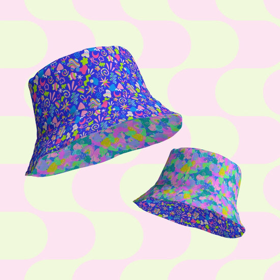 Two Neon Carnival/Funfetti reversible bucket hats from My Favourite Colour is Rainbow, with abstract floral and geometric patterns, are displayed on a pastel pink and green geometric background. One hat features vibrant blue flower designs; the other has a funfetti mix of multicolored shapes.