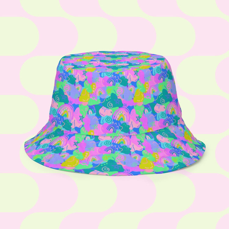 The Neon Carnival/Funfetti Reversible Bucket Hat from My Favourite Colour is Rainbow boasts a whimsical unicorn, rainbow, cloud, and star print on teal with a pastel funfetti-inspired polka dot pattern of light pink and pale yellow circles.