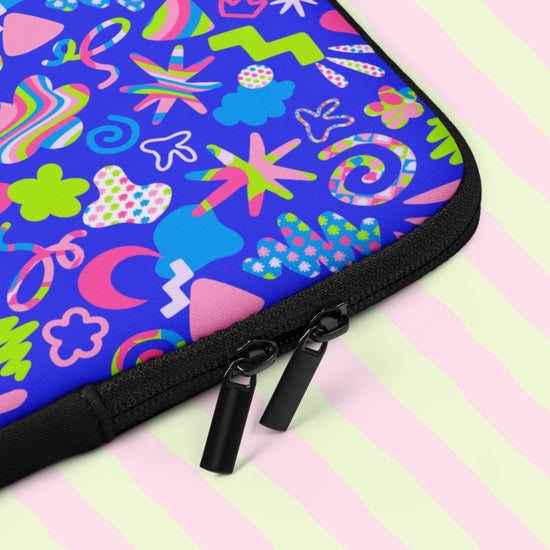 A closeup of the Neon Carnival Laptop Sleeve by My Favourite Colour is Rainbow featuring vibrant abstract shapes, lines and doodles in pink, green, blue and white on a bright blue background. It has two black zippers.  The print is on only one side of the laptop sleeve, the other side is black.