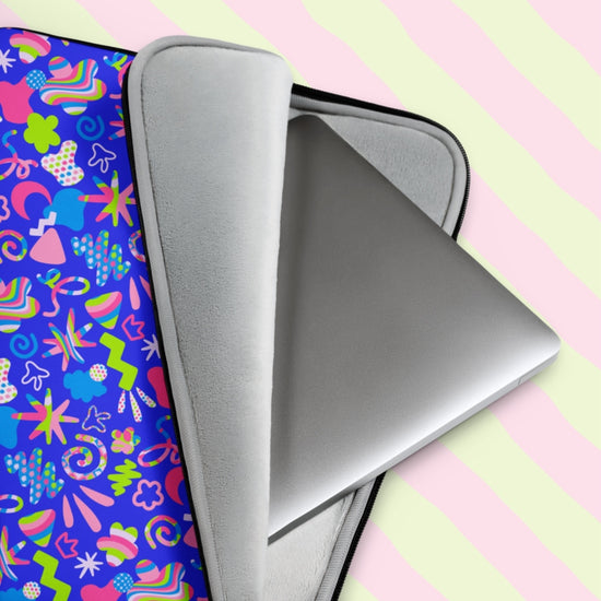 A silver laptop peeks from a vibrant My Favourite Colour is Rainbows Neon Carnival Laptop Sleeve, adorned with abstract shapes in blue, pink, and neon green against wavy pastel green and pink stripes, evoking a Neon Carnival vibe.