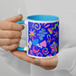 With painted nails, a person holds the Neon Carnival Mug by My Favourite Colour is Rainbow against a blue background. The mugs colourful, abstract design features stars, stripes, various geometric shapes and has a light blue interior.