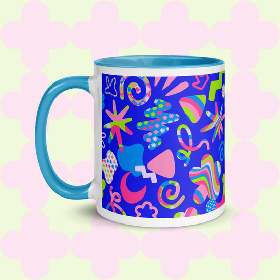 The Neon Carnival Mug by My Favourite Colour is Rainbow features vibrant abstract shapes and doodles in green, blue and white on a blue backdrop.  This version has a light blue handle and interior.