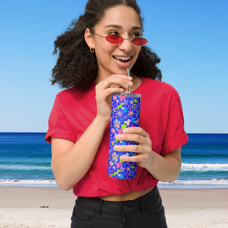 A woman in a red shirt and matching sunglasses smiles while sipping from a Neon Carnival Stainless Steel Tumbler by My Favourite Colour is Rainbow. 