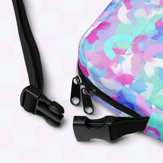 Close-up of the Pastel Rainbow Mini Crossbody Bag by My Favourite Colour is Rainbow, featuring an abstract pastel rainbow print in pink, purple, and turquoise. The image shows two black zippers and adjustable straps with a plastic buckle on a light background.