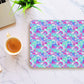 A laptop and coffee sit on a marble surface. Beside them is the Pastel Rainbow Mouse Pad by My Favourite Colour is Rainbow, showcasing pastel blues, purples, pinks, and greens in an abstract pattern. A small potted plant adds a touch of greenery.