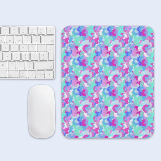 The Pastel Rainbow Mouse Pad by My Favourite Colour is Rainbow, featuring pink, blue, and purple abstract shapes, sits beside a white keyboard and mouse on a light blue surface.