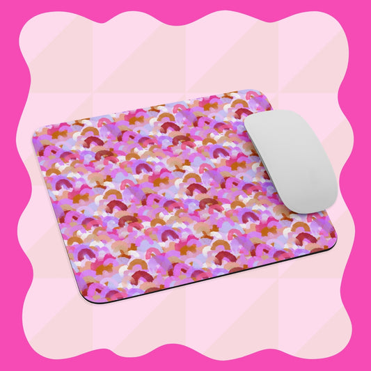 The Pink Rainbow Mouse Pad by My Favourite Colour is Rainbow features a colorful abstract design with shades of pink, purple, orange, and white, set against a pink and white checkered background with a wavy border. It comes with a white computer mouse.