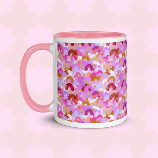 The Pink Rainbow Mug by My Favourite Colour is Rainbow is a ceramic mug featuring an abstract design of rainbow brushstrokes in shades of pink, burgundy, and gold with a pink light pink handle and interior.