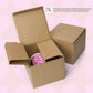 Two brown cardboard boxes sit on a pink patterned backdrop. One open box reveals a Pink Rainbow Mug by My Favourite Colour is Rainbow, featuring a vibrant pink and purple pattern. A text bubble in the corner mentions packaging variations for protection.