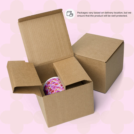 Two brown cardboard boxes sit on a pink patterned backdrop. One open box reveals a Pink Rainbow Mug by My Favourite Colour is Rainbow, featuring a vibrant pink and purple pattern. A text bubble in the corner mentions packaging variations for protection.