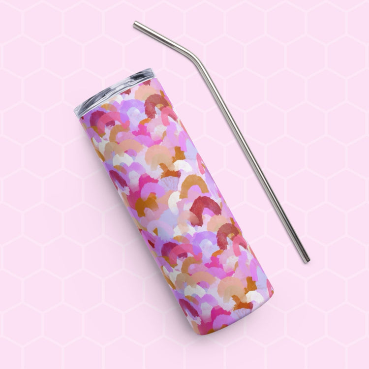 The Pink Rainbow Stainless Steel Tumbler by My Favourite Colour is Rainbow features a colorful abstract pattern of pink, purple, and orange shapes. It rests on a pink hexagonal-patterned background with a metal straw placed beside it.