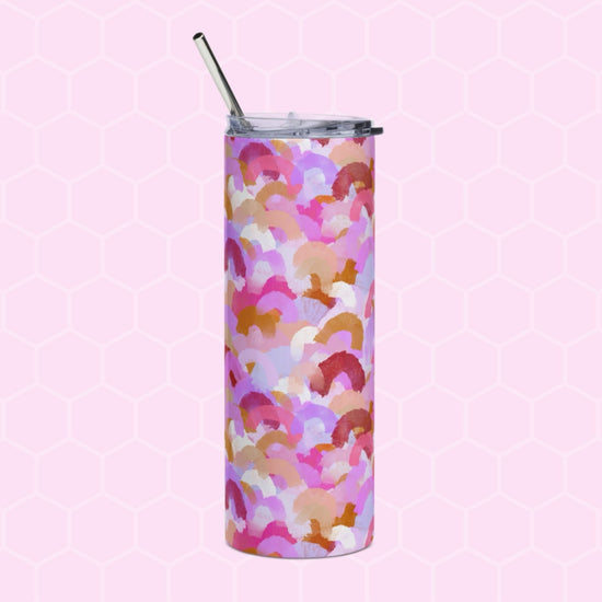 A Pink Rainbow Stainless Steel Tumbler from My Favourite Colour is Rainbow, featuring a vibrant abstract design in pink, orange, and purple shades with a metal straw, rests on a pink hexagonal patterned background.