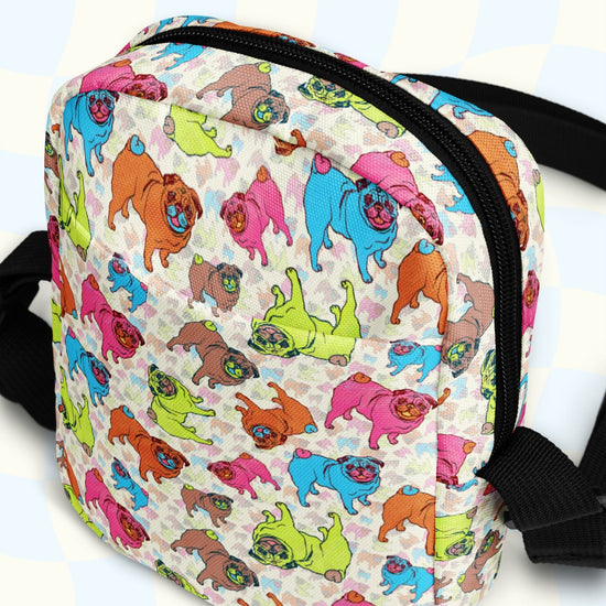 The Pugalicious Mini Crossbody Bag by My Favourite Colour is Rainbow features cartoon pugs in vibrant orange, pink, blue, and green on a light background. This water-resistant bag has adjustable black straps and a sleek black zipper to enhance its playful design.