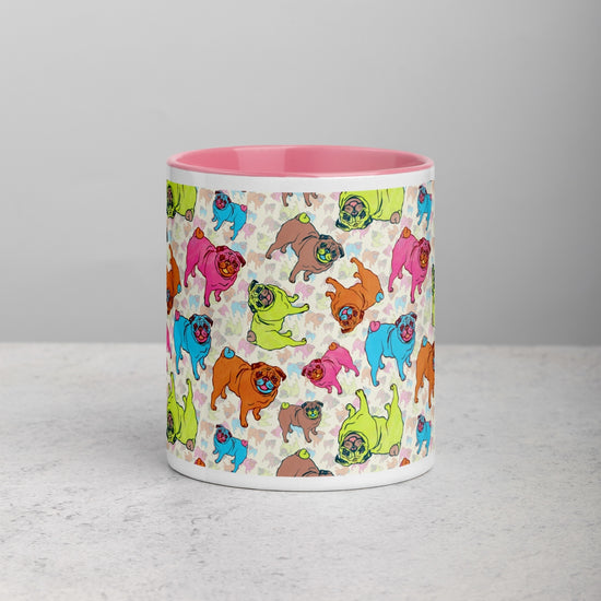 Front view of the Pugalicious Mug by My Favourite Colour is Rainbow, a vibrant delight for pug enthusiasts. Featuring cartoon pugs in pink, blue, green, and brown, and a pink interior, it’s shown on a light grey bench.