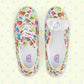 The Pugalicious Canvas Sneakers by My Favourite Colour is Rainbow showcase a delightful dinosaur pattern in green, pink, and blue on a light background. Displayed from above on a pale yellow surface with star designs, these lace-up shoes radiate charm and whimsy.