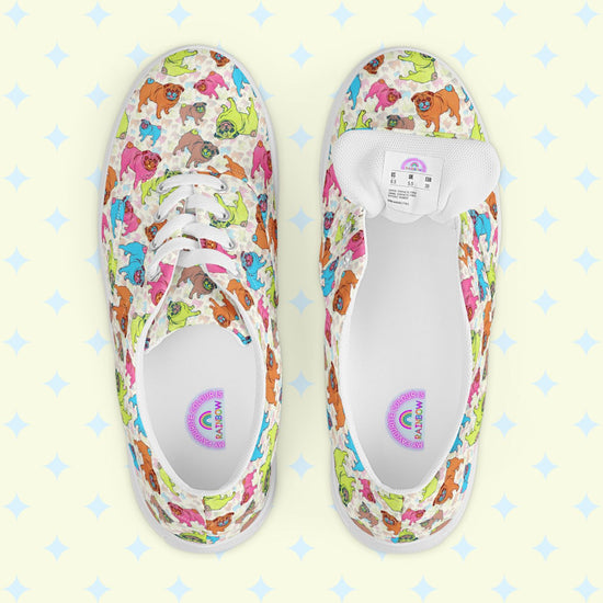 The Pugalicious Canvas Sneakers by My Favourite Colour is Rainbow showcase a delightful dinosaur pattern in green, pink, and blue on a light background. Displayed from above on a pale yellow surface with star designs, these lace-up shoes radiate charm and whimsy.