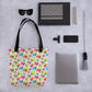 The Pugalicious Tote Bag by My Favourite Colour is Rainbow lies flat with sunglasses, two notebooks, three black pens, a smartphone with a lens attachment, a gray tassel, and a closed laptop on a gray speckled surface.