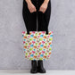 A person showcases the spacious, trendy Pugalicious Tote Bag by My Favourite Colour is Rainbow, adorned with cartoon pugs, while standing against a grey textured wall. They are dressed in black pants and boots.